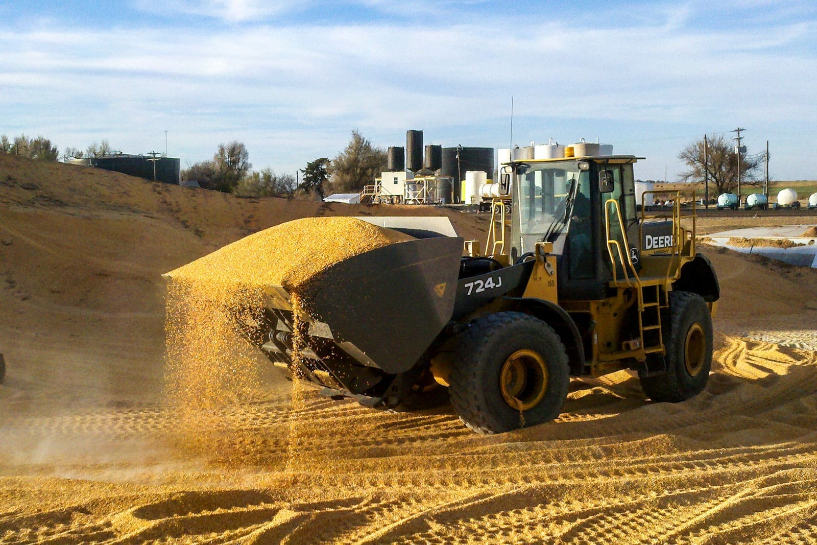 Wheel loader using a Dymax roll out bucket to unload corn onto a pile in an agricultural material handling yard