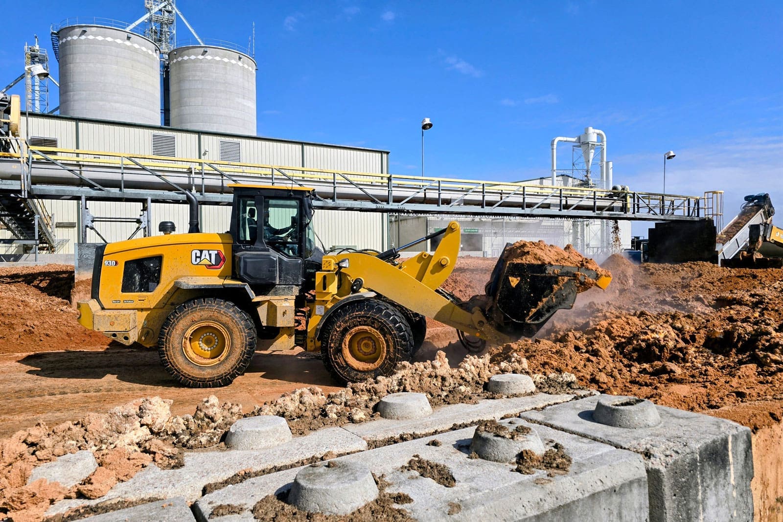 Cat wheel loader operating with a Dymax roll out bucket while moving and dumping wet distillers grain (WDG)