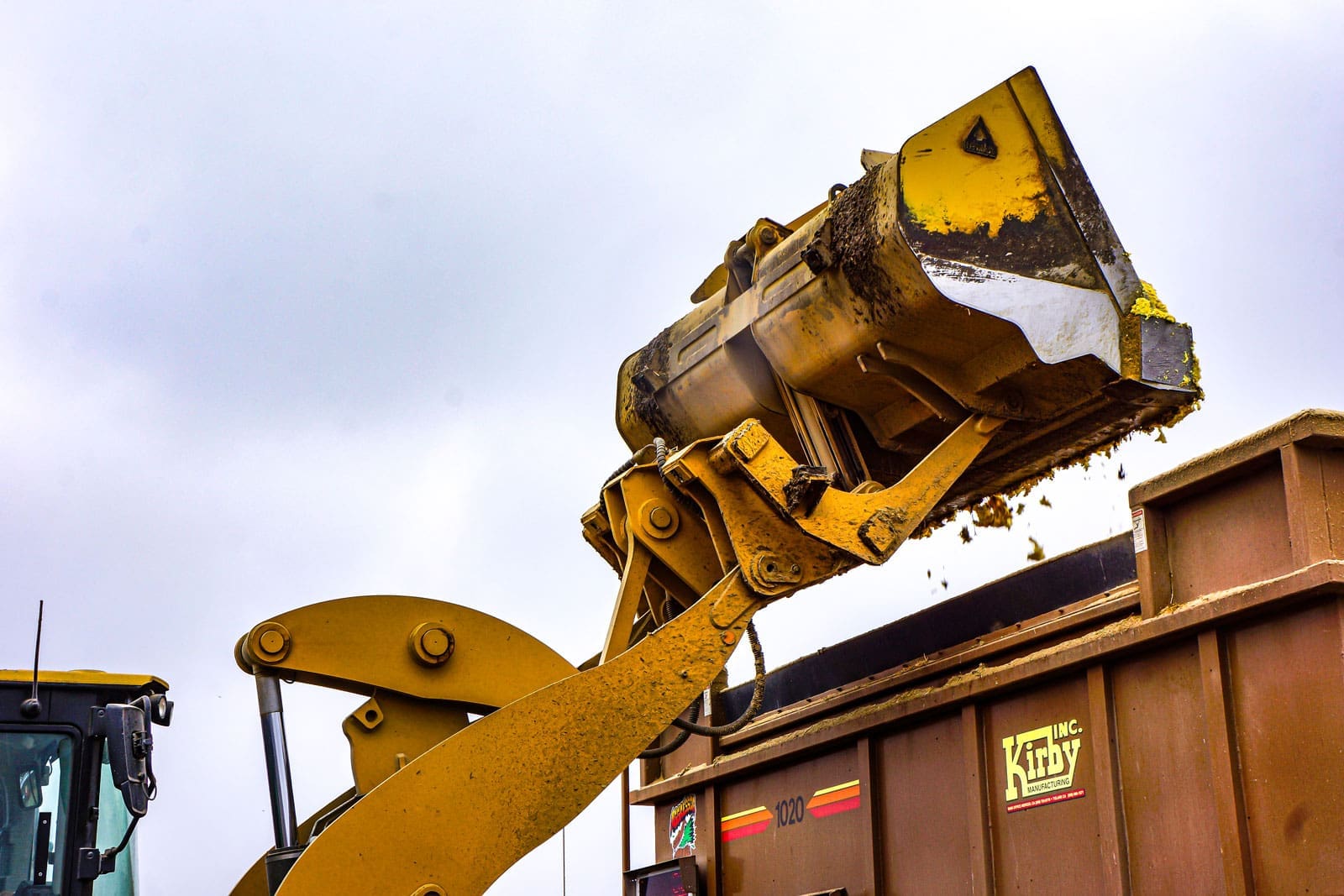 Dymax roll out bucket on a wheel loader dumping material into a tall-sided container for high dump clearance