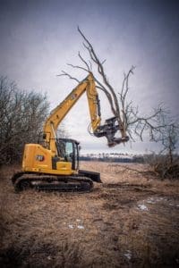 Cat 315 Excavator lifting a large branch after cutting it with a tree shear.