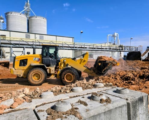 A CAT 930 high lift loader moves abrasive WDG at an ethanol processing plant, showing the heavy-duty Dymax bucket in action.