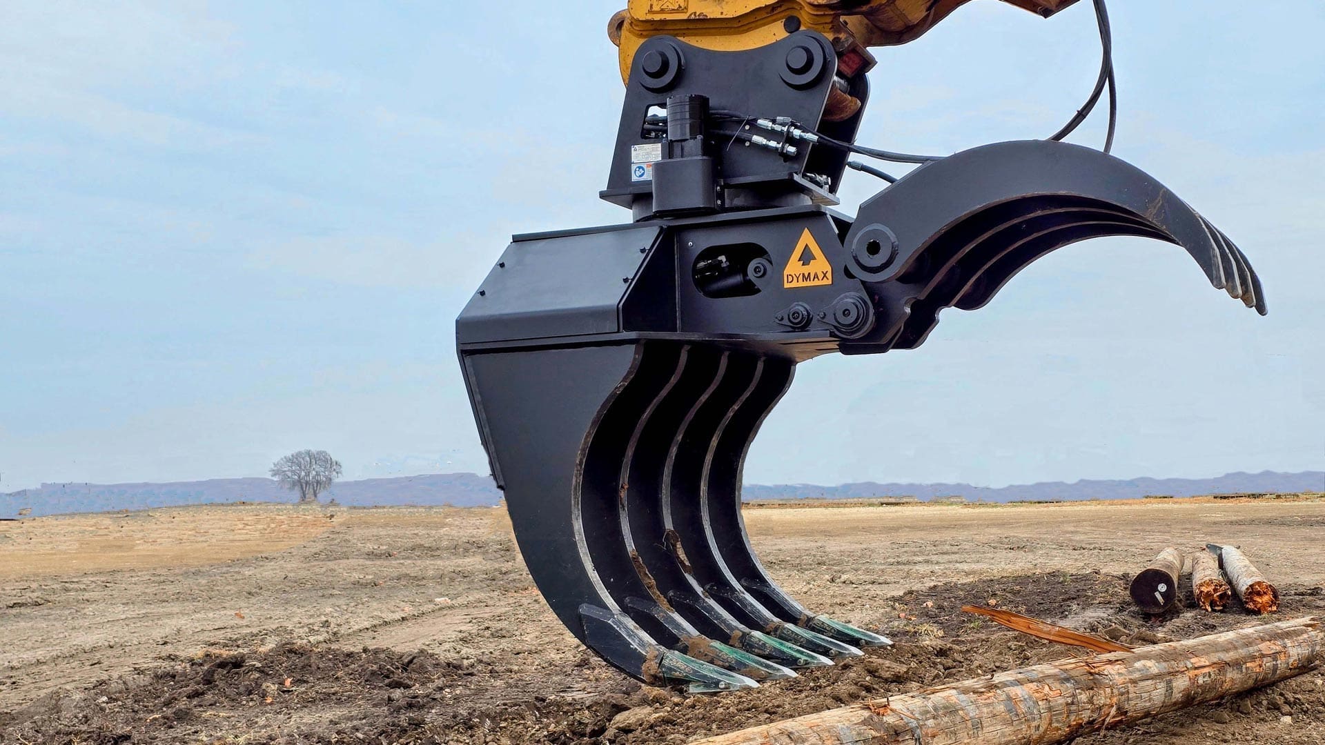 Dymax IronClaw 360° excavator grapple rake lifting and rotating logs on jobsite